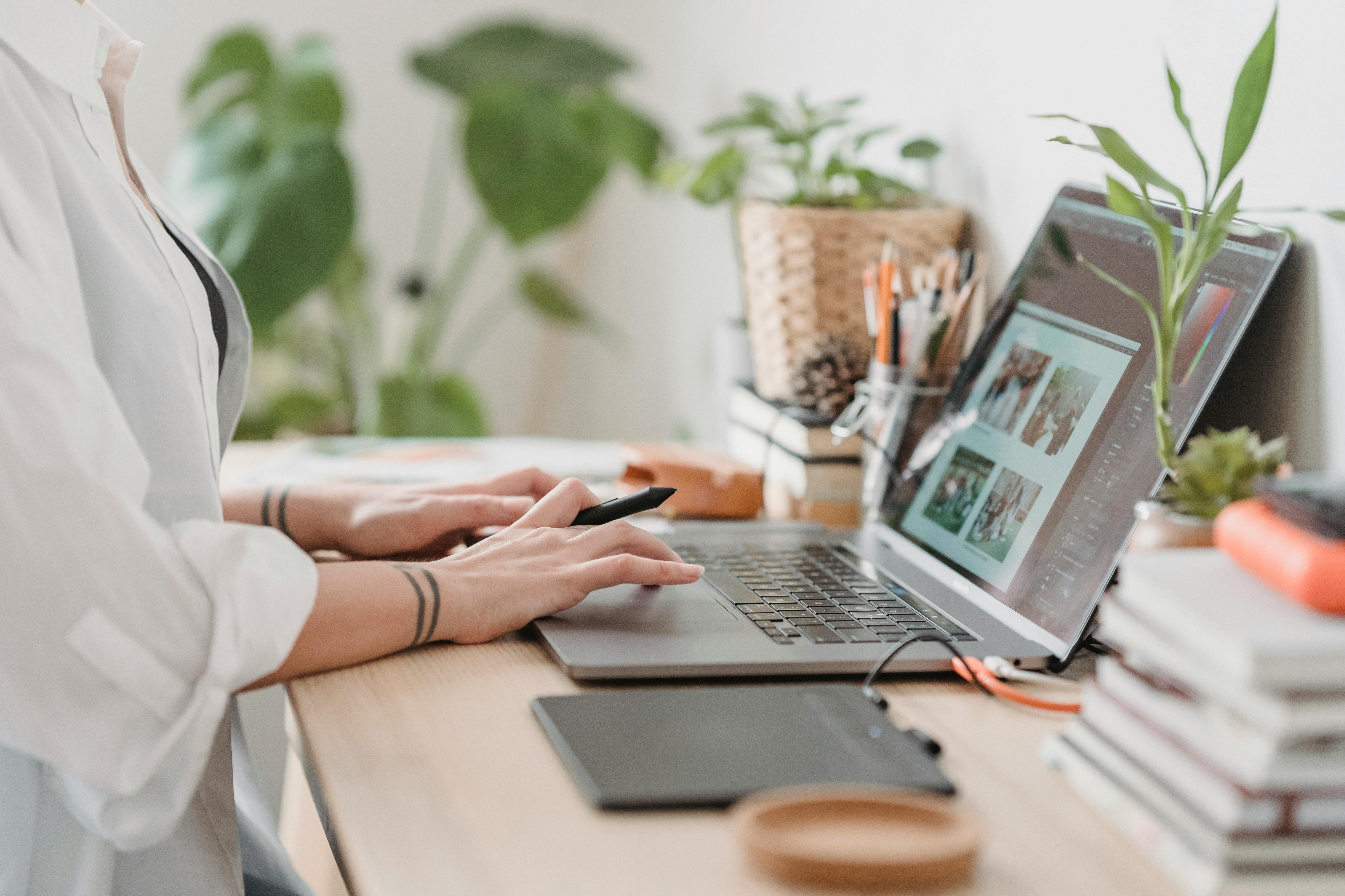 Person working on a laptop at a desk with plants and books in the background