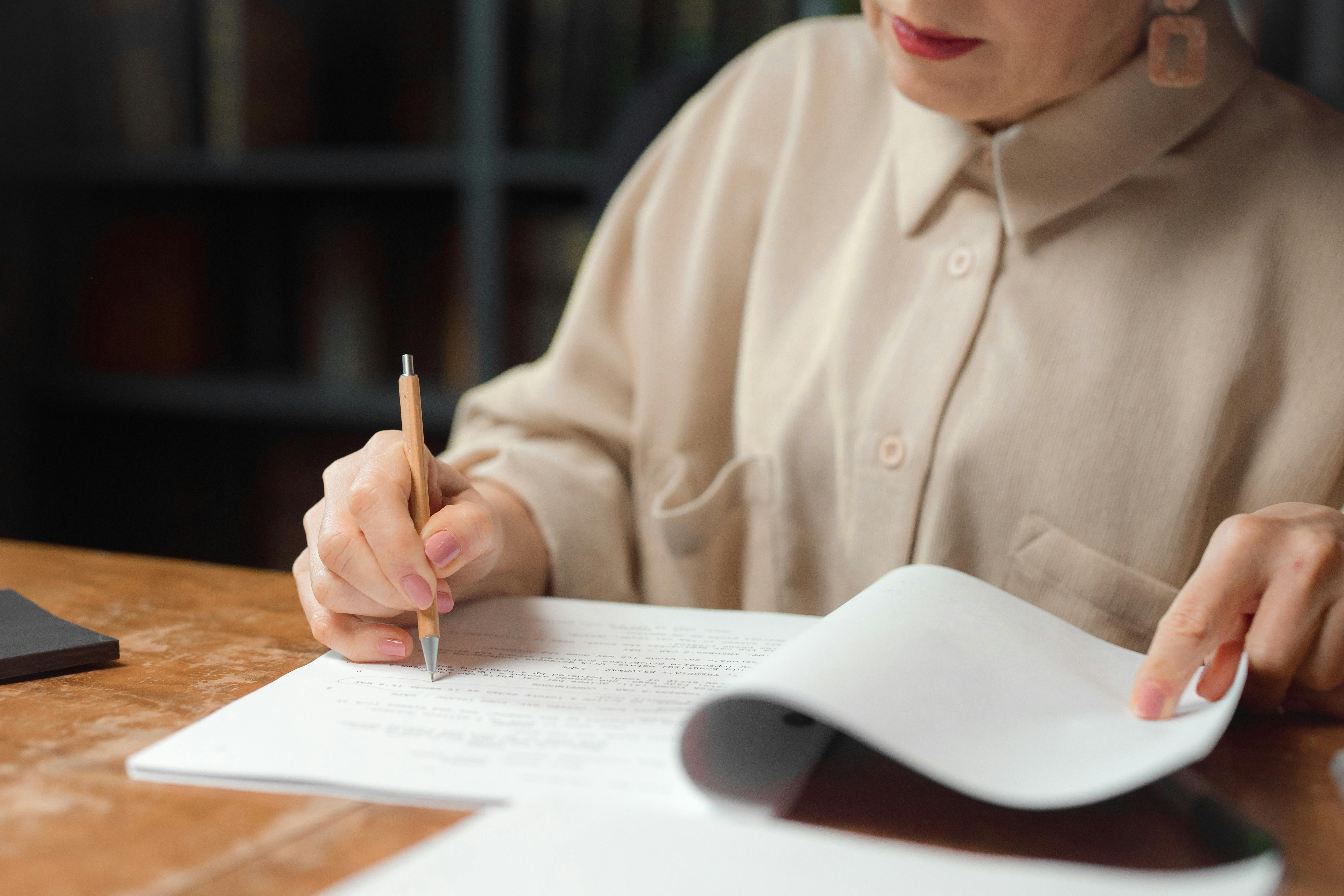 Person writing on a piece of paper with a pen at a desk.
